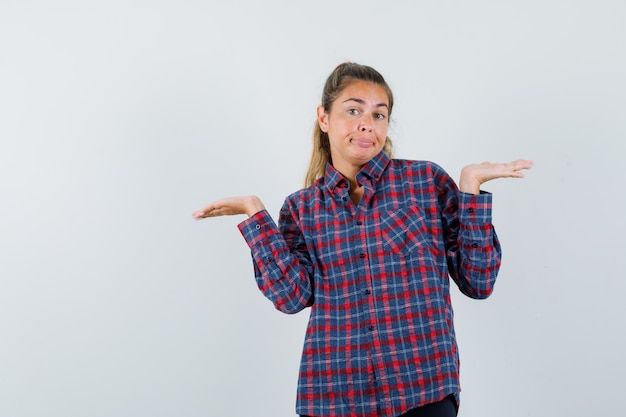 Foto gratuita giovane donna che scrolla le spalle in camicia a quadri e sembra perplessa