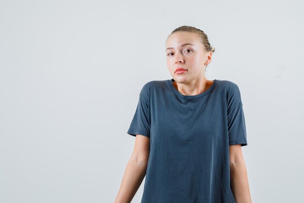 Young woman shrugging shoulders in helpless manner in gray t-shirt and looking confused