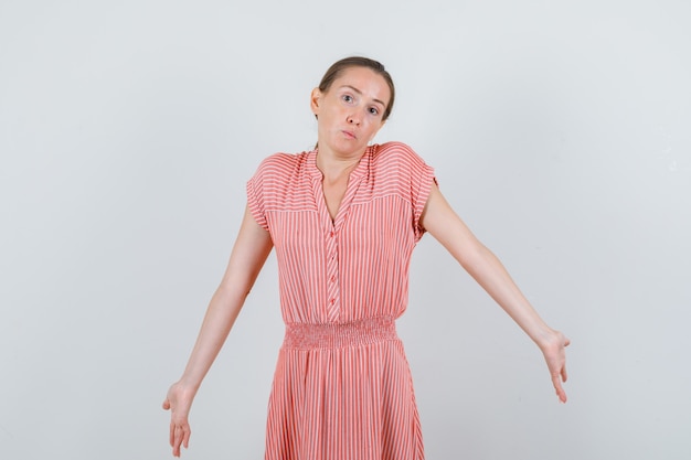 Young woman shrugging and showing helpless gesture in striped dress , front view.