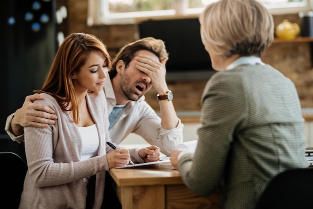 Young woman signing a contract with insurance agent while her husband is disagreeing with her decision.