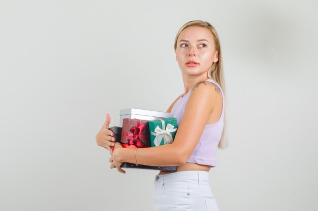 Young woman in singlet, mini skirt looking aside and holding gift boxes