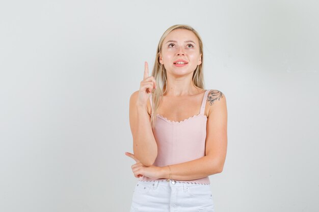 Young woman in singlet, mini skirt looking up with finger up and looking joyful