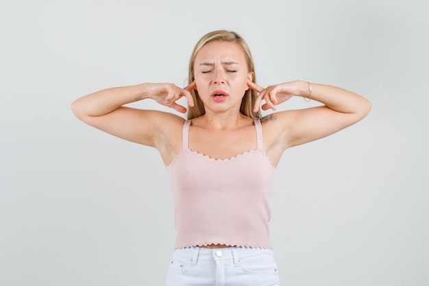 Foto gratuita giovane donna in canottiera, minigonna tappando le orecchie con le dita e guardando disgustata