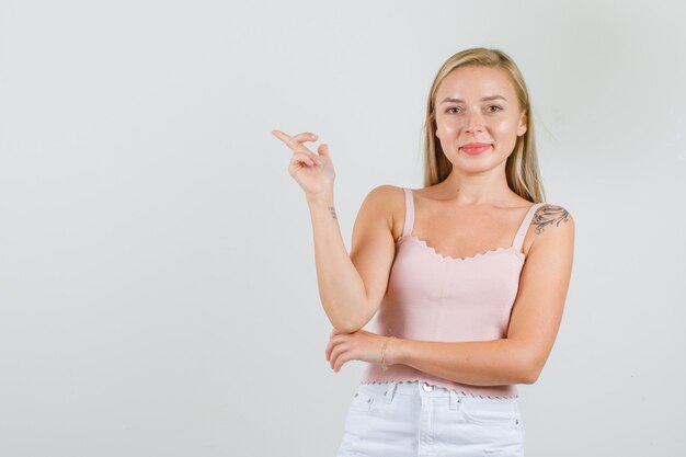 Young woman in singlet, mini skirt pointing away and smiling