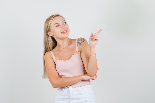 Young woman in singlet, mini skirt pointing away and smiling