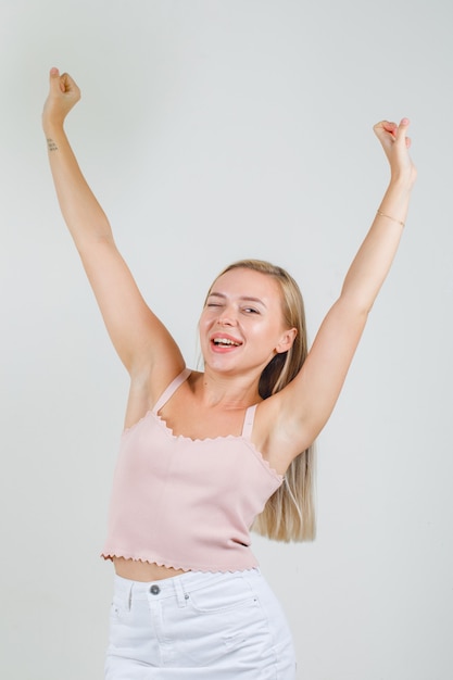 Foto gratuita giovane donna in canottiera, minigonna alzando le braccia e guardando felice