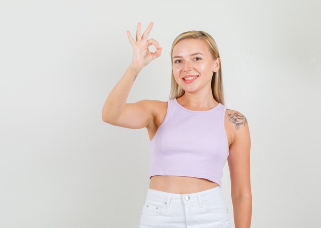 Young woman in singlet, mini skirt showing ok sign and looking cheerful