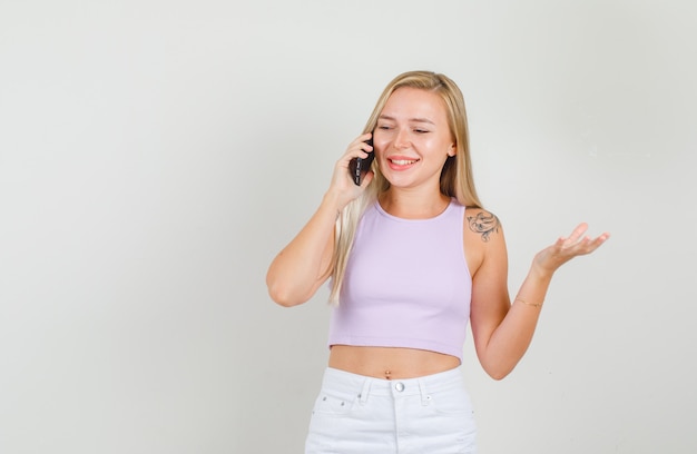 Young woman in singlet, mini skirt talking on phone and smiling