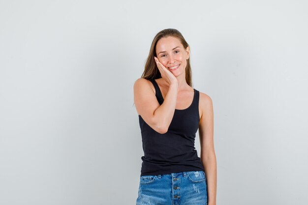 Young woman in singlet, shorts holding palm on cheek and smiling