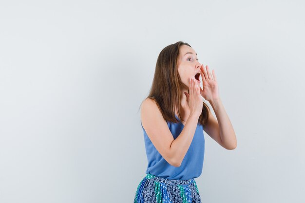 Young woman in singlet, skirt telling secret with hands near open mouth , front view.