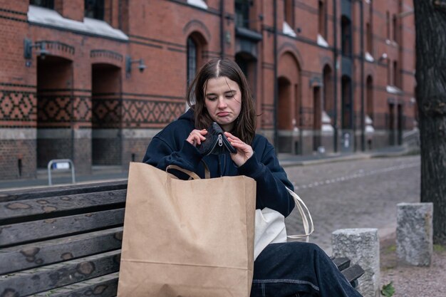 若い女性はお金の不足の空の財布の概念でベンチに座っています