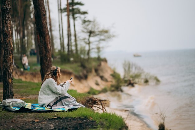 한 젊은 여성이 숲 근처의 작은 호수 기슭에 앉아 있다