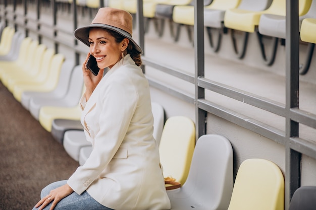 Молодая женщина сидит на местах арены и разговаривает по телефону