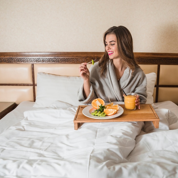 Young woman sitting on bed having fresh nutritious breakfast on bed