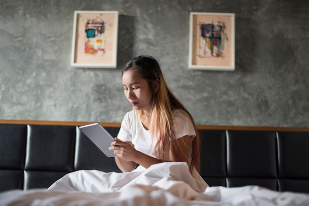 Young woman sitting on the bed and using her tablet pc