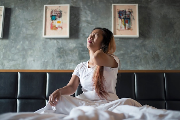 Young woman sitting on the bed with neck pain after wake up