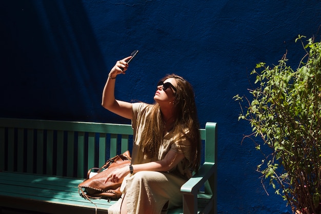 Young woman sitting on bench taking selfie