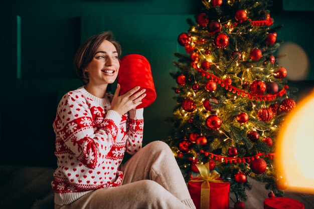 빨간 상자와 함께 크리스마스 트리 옆에 앉아 젊은 여자