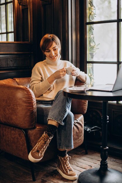 Молодая женщина сидит в кафе, пьет кофе и работает за компьютером