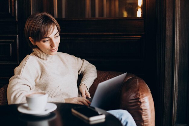 Молодая женщина сидит в кафе, пьет кофе и работает за компьютером