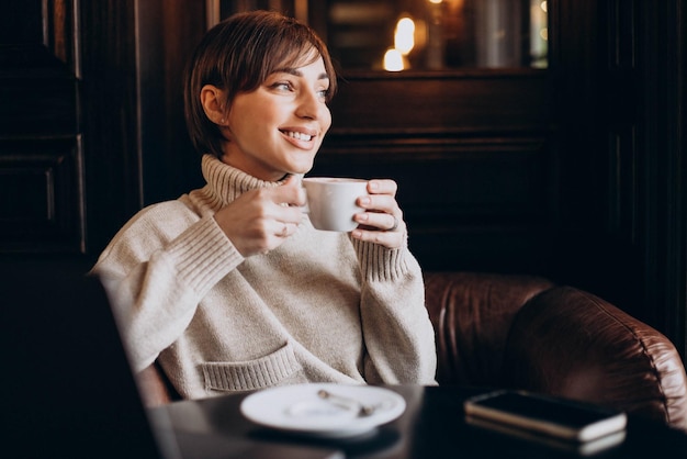 Giovane donna seduta in un caffè a bere caffè e lavorare su un computer