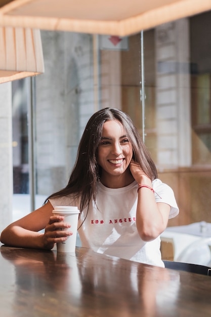Foto gratuita giovane donna che si siede nel caffè che tiene la tazza di caffè a gettare al tavolo