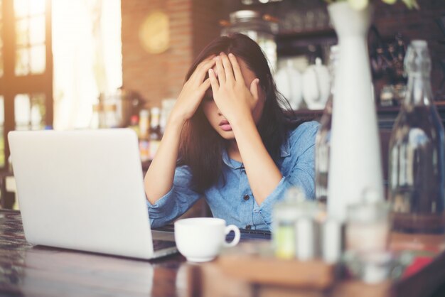 WORのためのストレスの多い彼女のラップトップとカフェに座って若い女性、