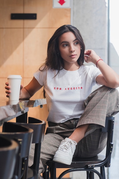 Молодая женщина, сидя в кресле, держа одноразовые чашки кофе за столом