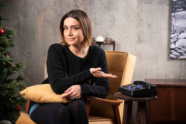 Young woman sitting on chair showing telephone.