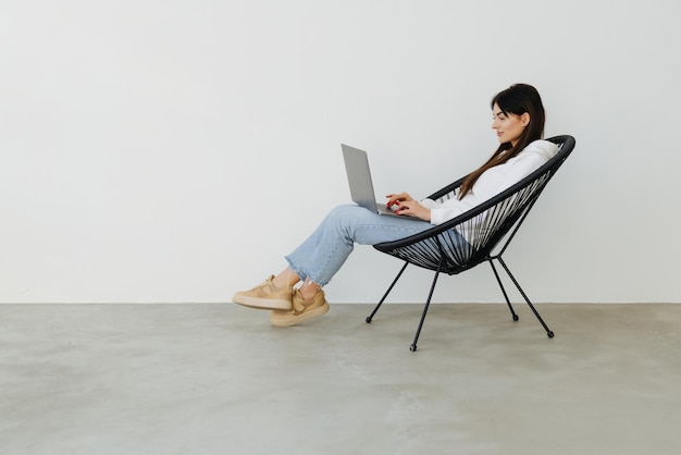 집에서 노트북을 들고 의자에 앉아 있는 젊은 여성