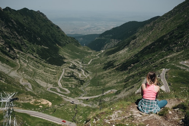 Transfegerasan 산악 도로에서 위에서 찾고 절벽 가장자리에 앉아 젊은 여자.