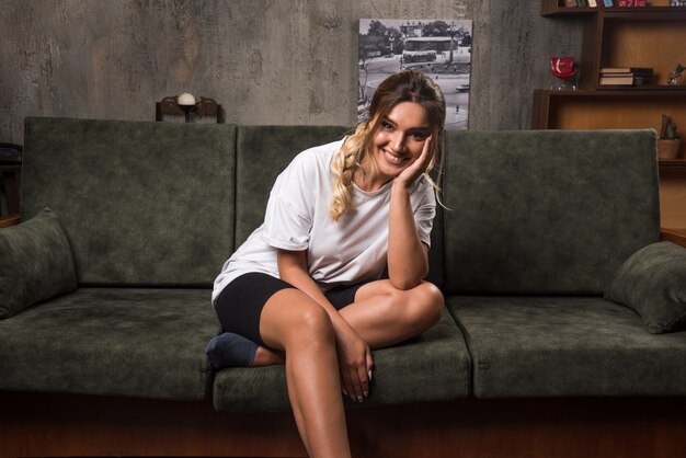 Young woman sitting on couch looking front while smiling.