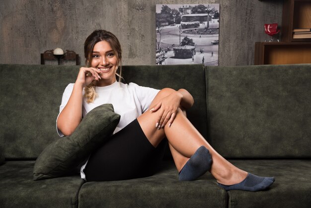 Young woman sitting on couch looking front while smiling.