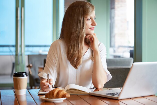 Young woman sitting at desk holding pen and looking at the window