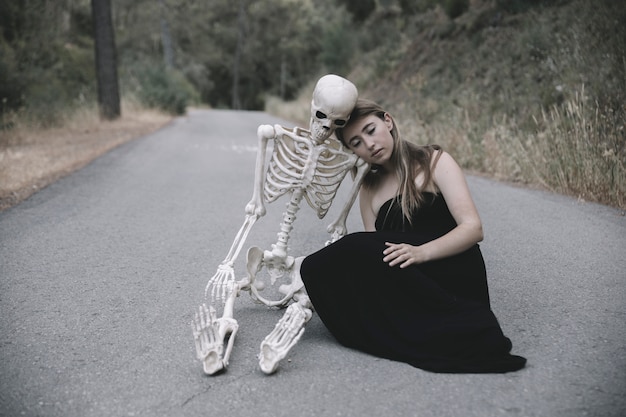 Молодая женщина, сидя на пустой дороге с скелетом