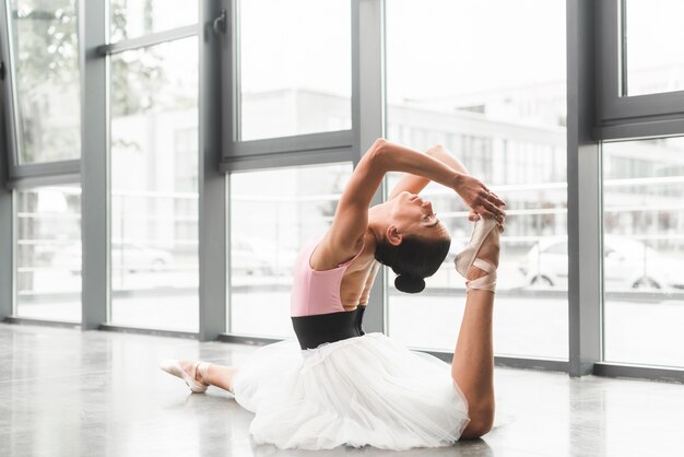 Young woman sitting on floor practicing ballet dance in dance studio