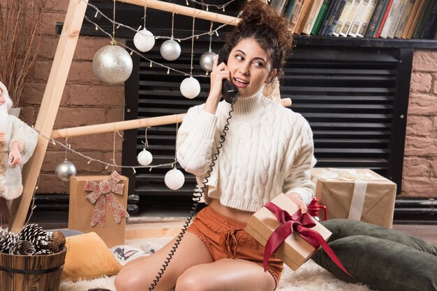 A young woman sitting on fluffy carpet and speaking on telephone 