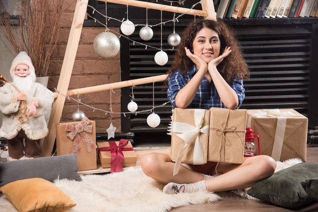 Young woman sitting on fluffy carpet with boxes of Christmas presents 