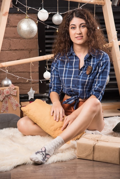 Young woman sitting on fluffy carpet with Christmas decorations 