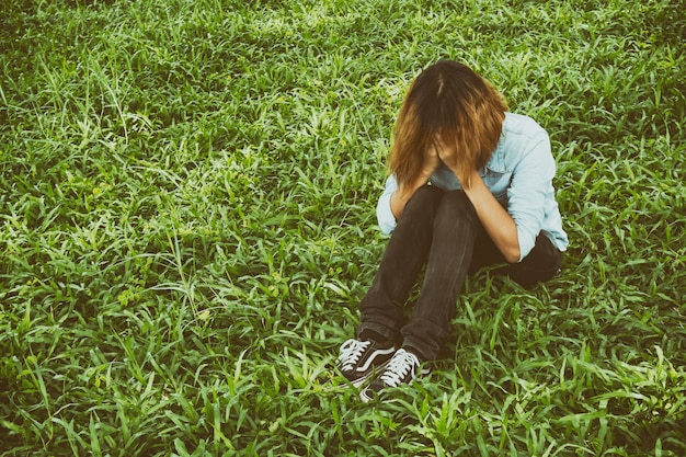 泣いて草の上に座っている若い女性