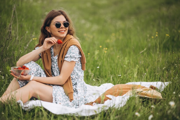 Молодая женщина сидит на траве и ест клубнику