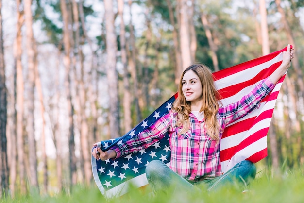 草の上に座っているとアメリカの国旗を保持している若い女性
