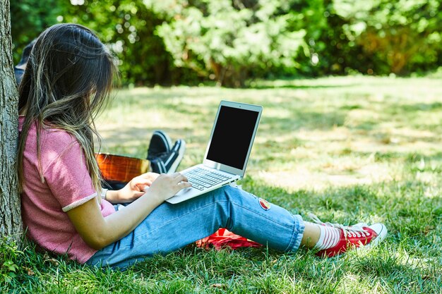노트북을 사용하는 동안 푸른 잔디에 앉아 젊은 여자