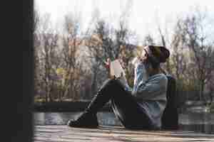 Free photo young woman sitting on jetty above the lake and reading a book