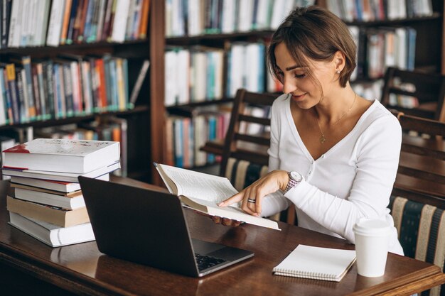 本とコンピューターを使用して図書館に座っている若い女性