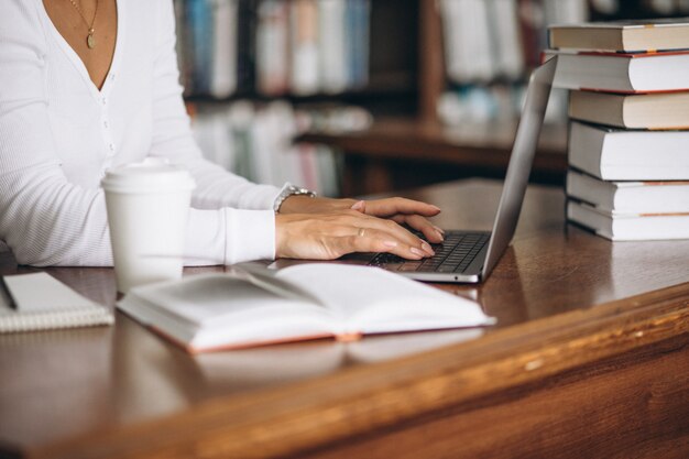 Young woman sitting at the library using books and computer