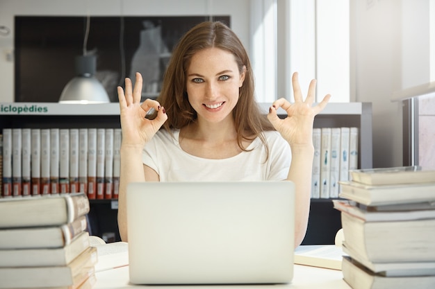 Free photo young woman sitting in library with laptop