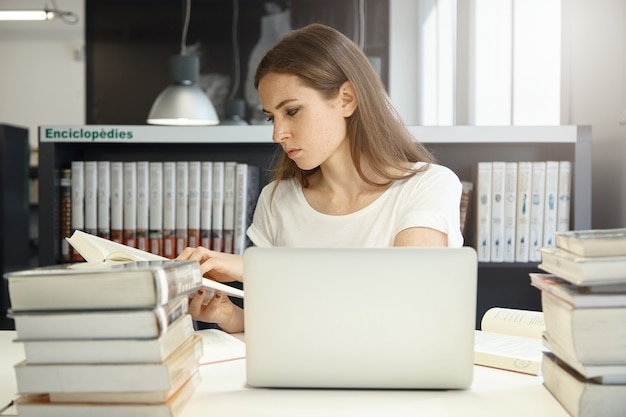 Giovane donna seduta in libreria con il computer portatile