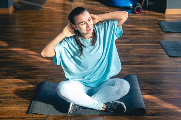 Foto gratuita giovane donna seduta su un tappetino in un centro fitness che fa yoga e stretching