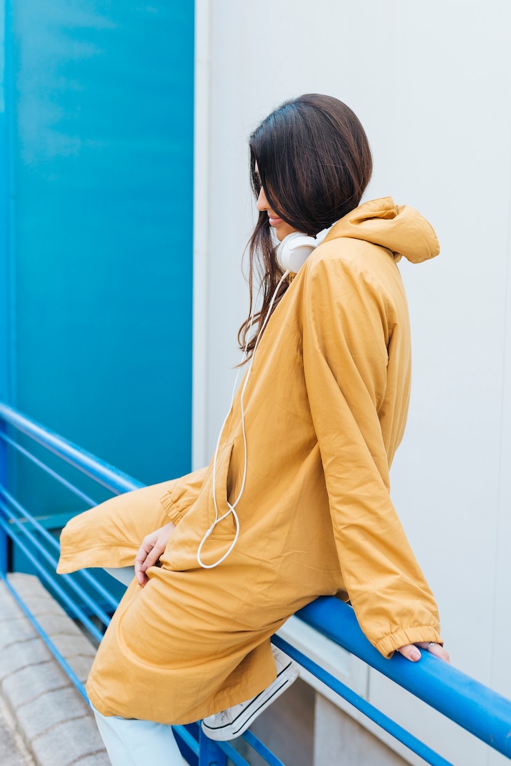 免費 Photo 一位坐在金属蓝色栏杆上的年轻女人,脖子上戴着耳机